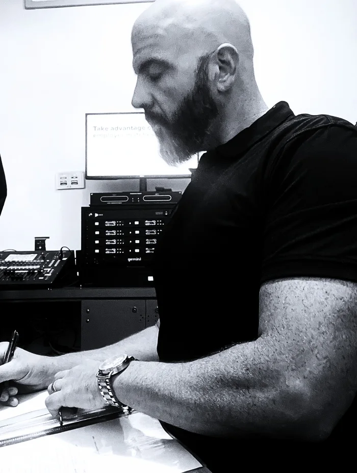 Brian Black marking up a run sheet beside an audio mixer and a rack of wireless microphones